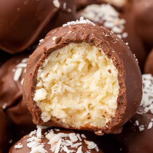 A coconut ball covered in dark chocolate that has a bite taken out of it.