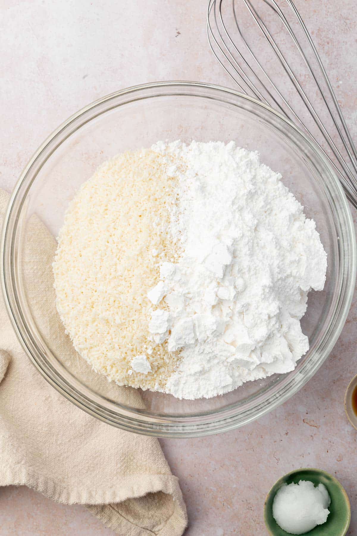 A glass mixing bowl with coconut flakes and powdered sugar before mixing together.