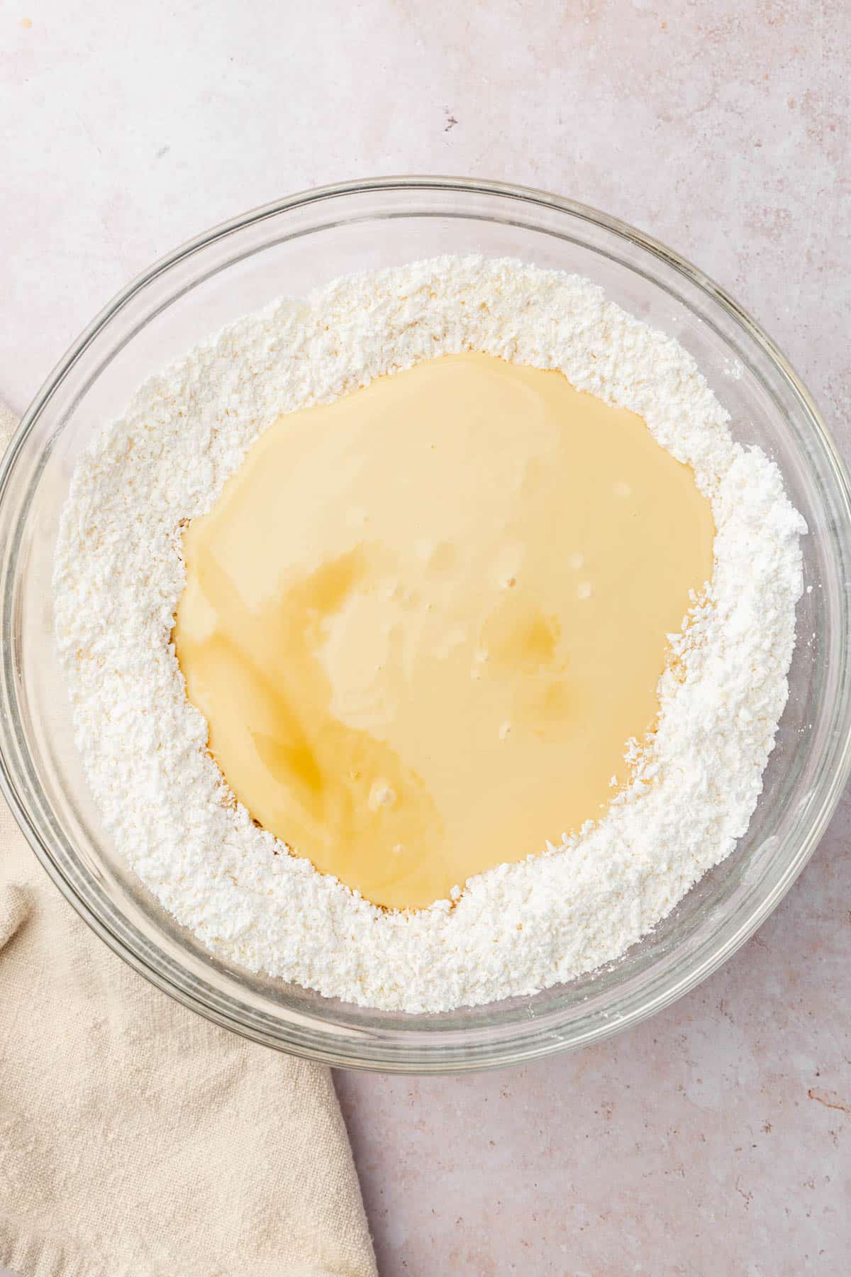 A bowl of shredded coconut flakes and powdered sugar topped with sweetened condensed milk and vanilla extract before mixing together.