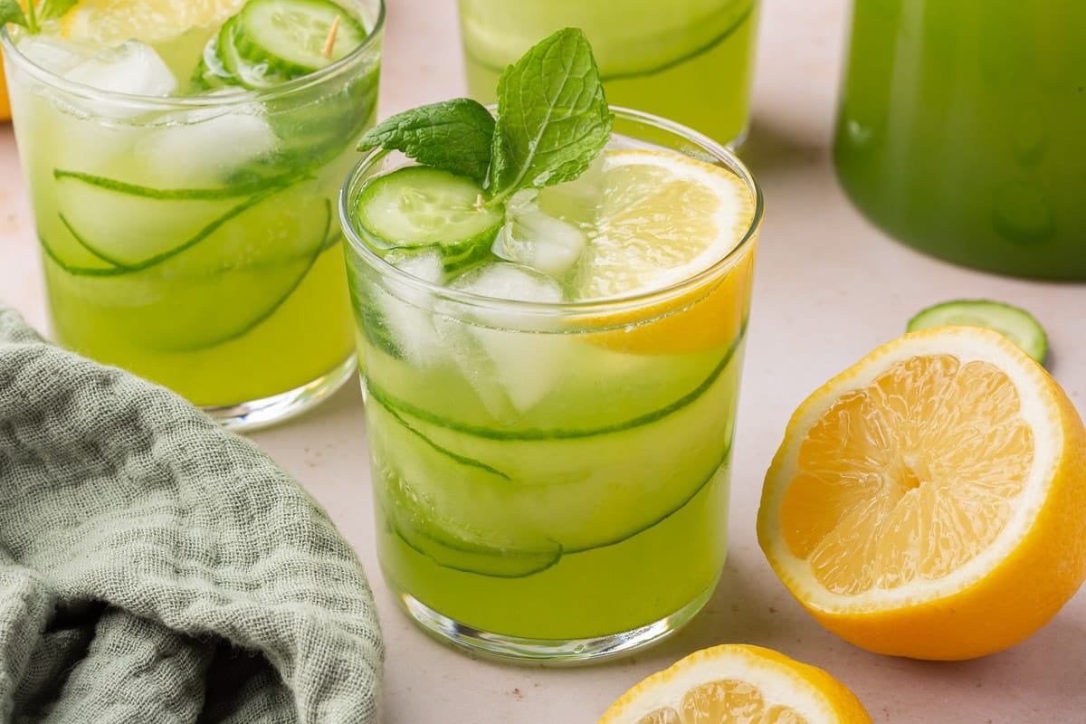 Multiple glasses of cucumber lemonade with fresh mint with a lemon half on the side.
