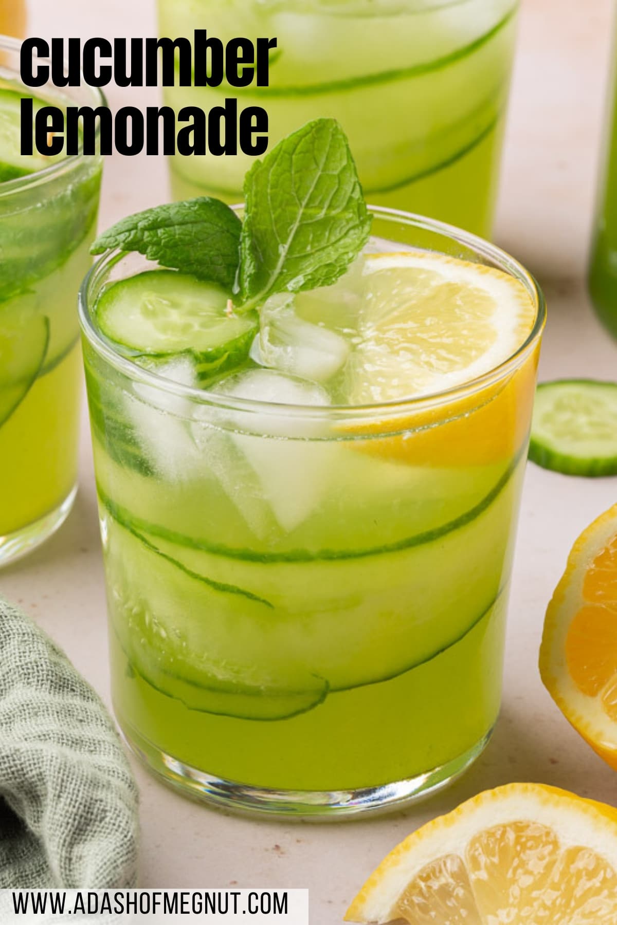 A glass of cucumber lemonade with fresh mint, ice cubes, lemon wedges, and cucumber ribbons.