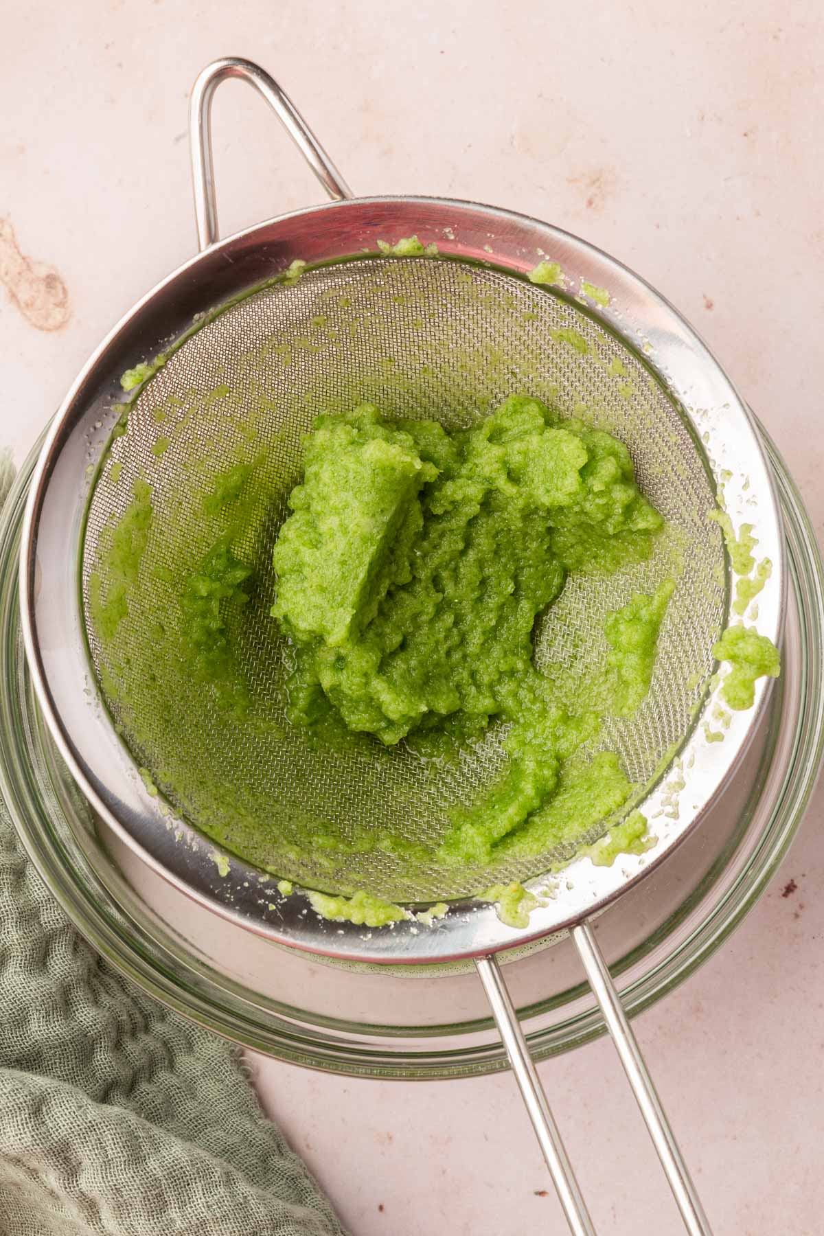 A glass bowl with a fine-mesh sieve on top of it with cucumber pulp.