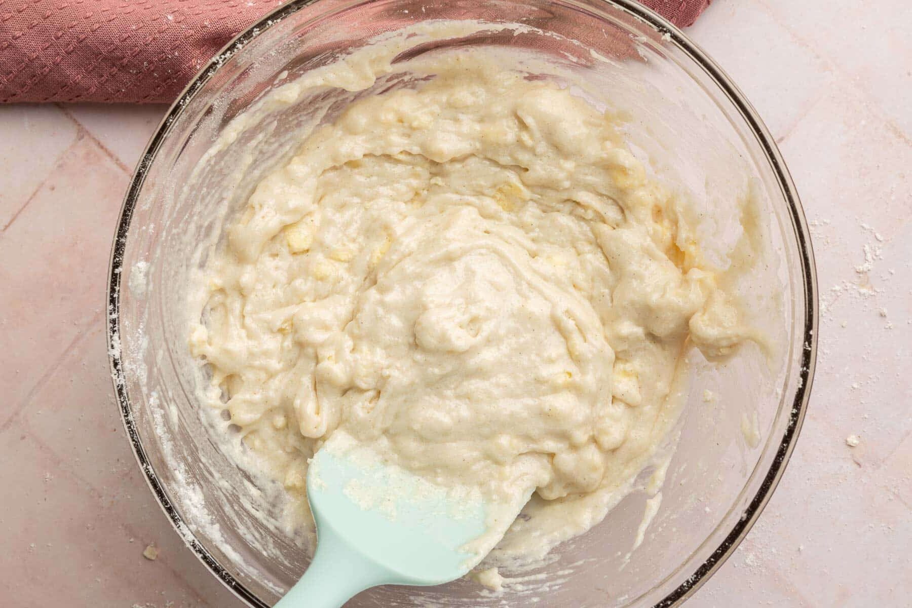 A glass mixing bowl with a gluten-free cobbler batter and a blue spatula.