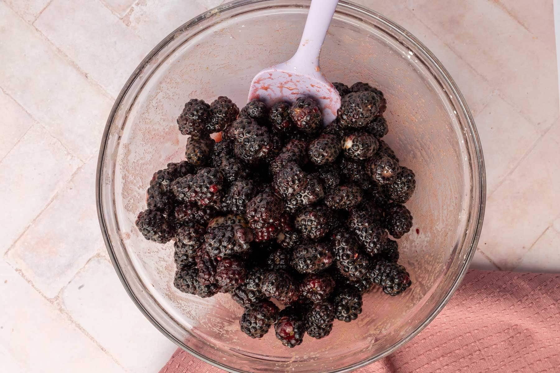 A glass mixing bowl with blackberries that have been tossed with granulated sugar, cornstarch, cinnamon, and lemon juice.