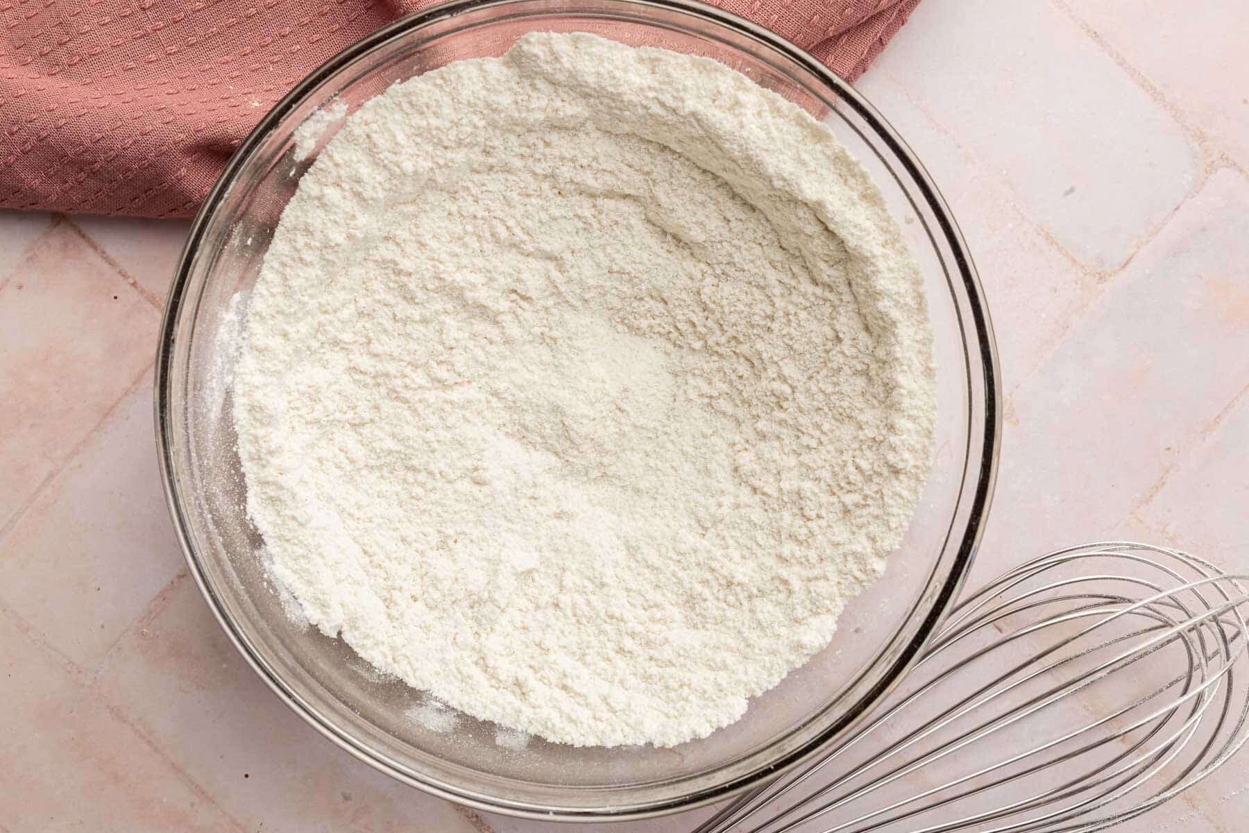 A glass mixing bowl with a gluten-free flour blend in it with a whisk to the side.