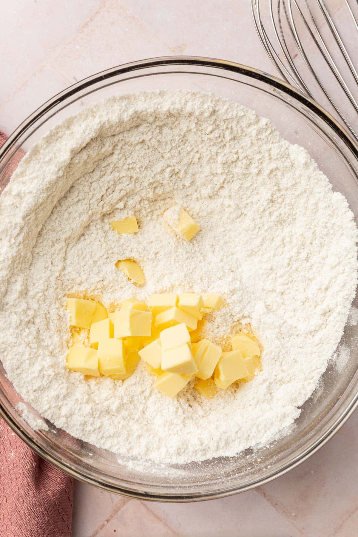 A glass mixing bowl with a gluten-free flour blend topped with small cubes of vegan butter.