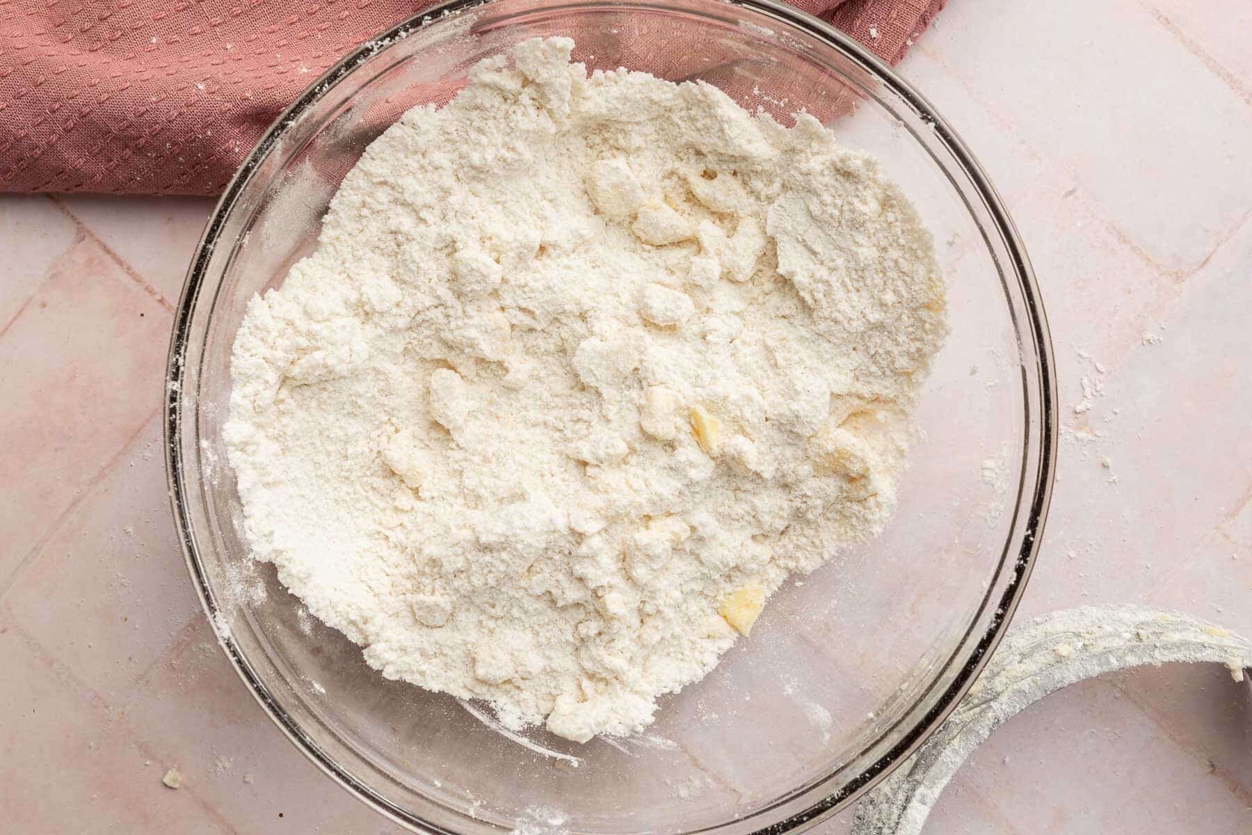 A glass mixing bowl with vegan butter cut into gluten-free flour with a pastry cutter to the side.