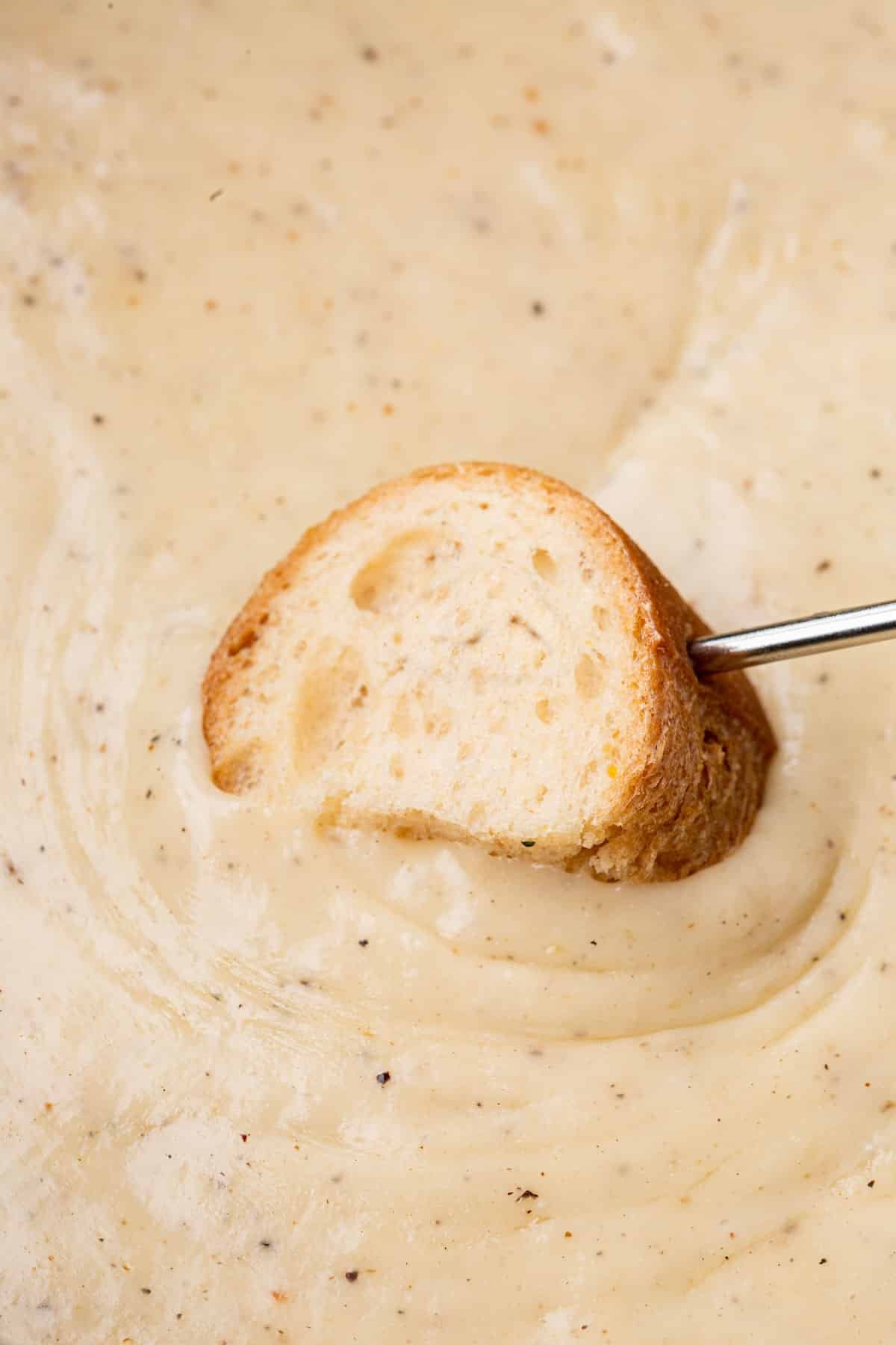 A skewered piece of gluten-free bread dipped into gluten-free cheese fondue.