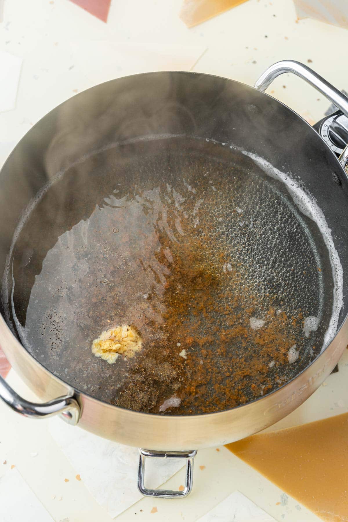 An electric fondue pot that has simmering white wine with mustard powder, nutmeg, and black pepper on top of it.