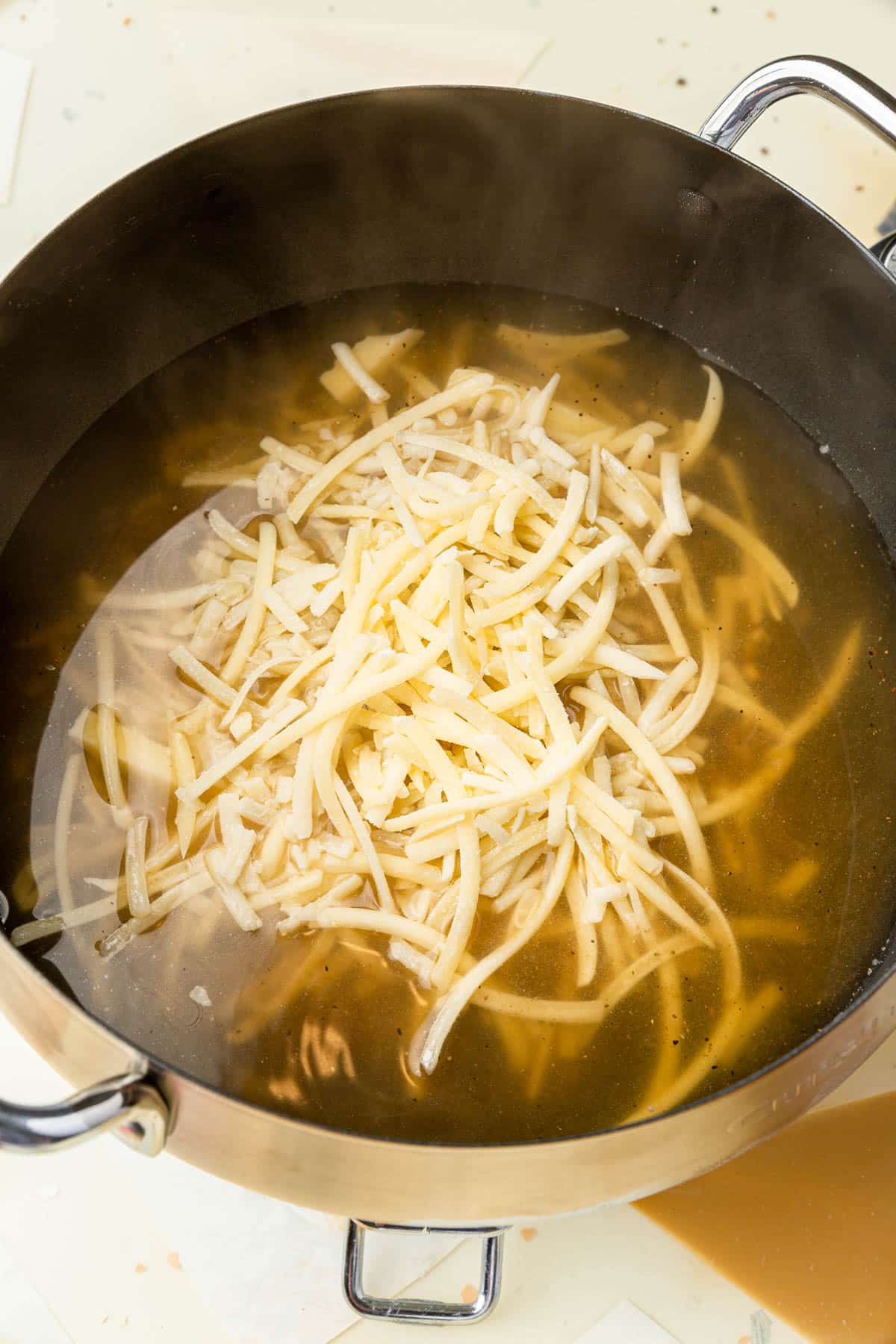 An electric fondue pot with a white wine and spice mixture that has shredded cheese in it that has not yet melted.