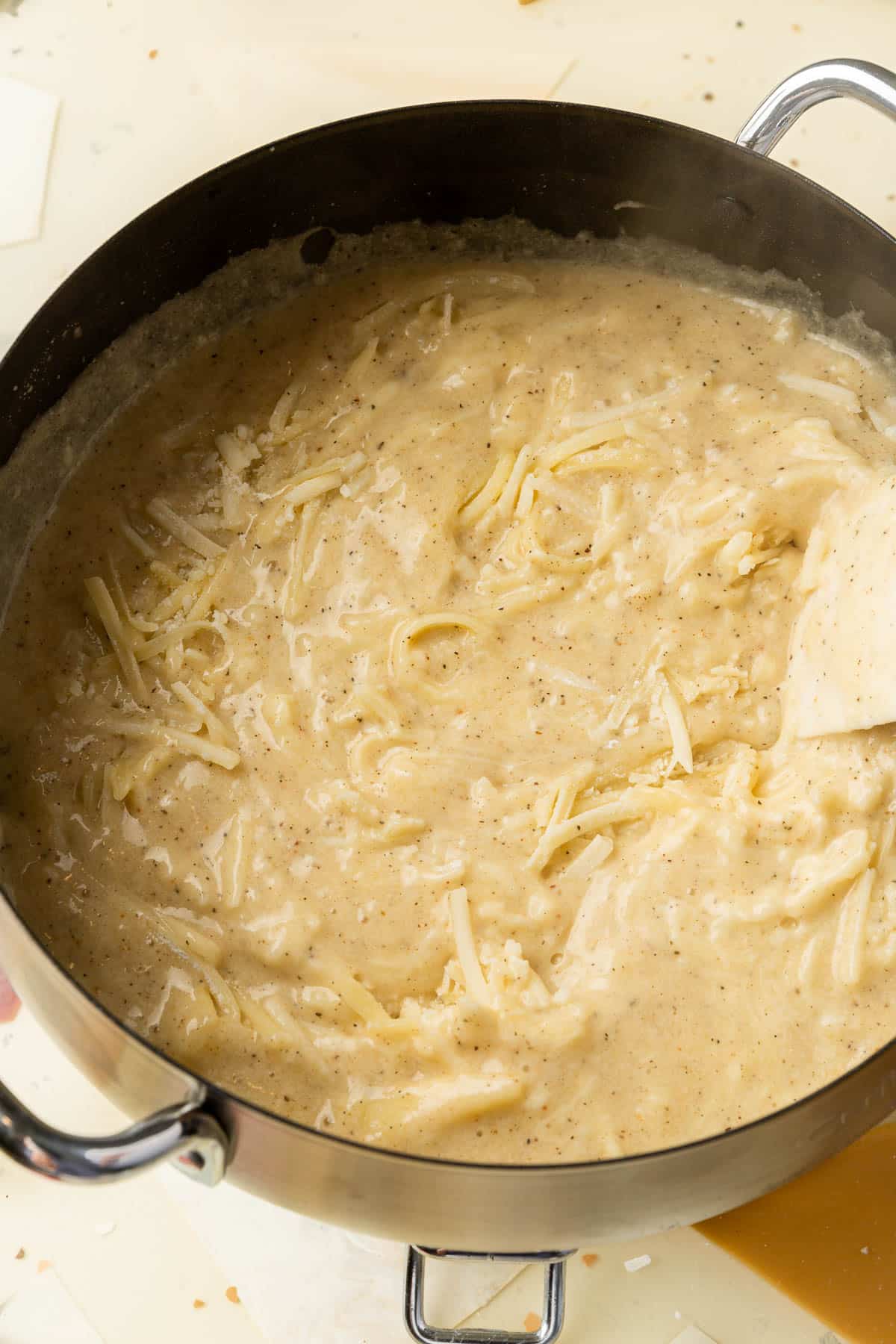 A fondue pot with shredded cheese that is melting into the cheese sauce with a rubber spatula.