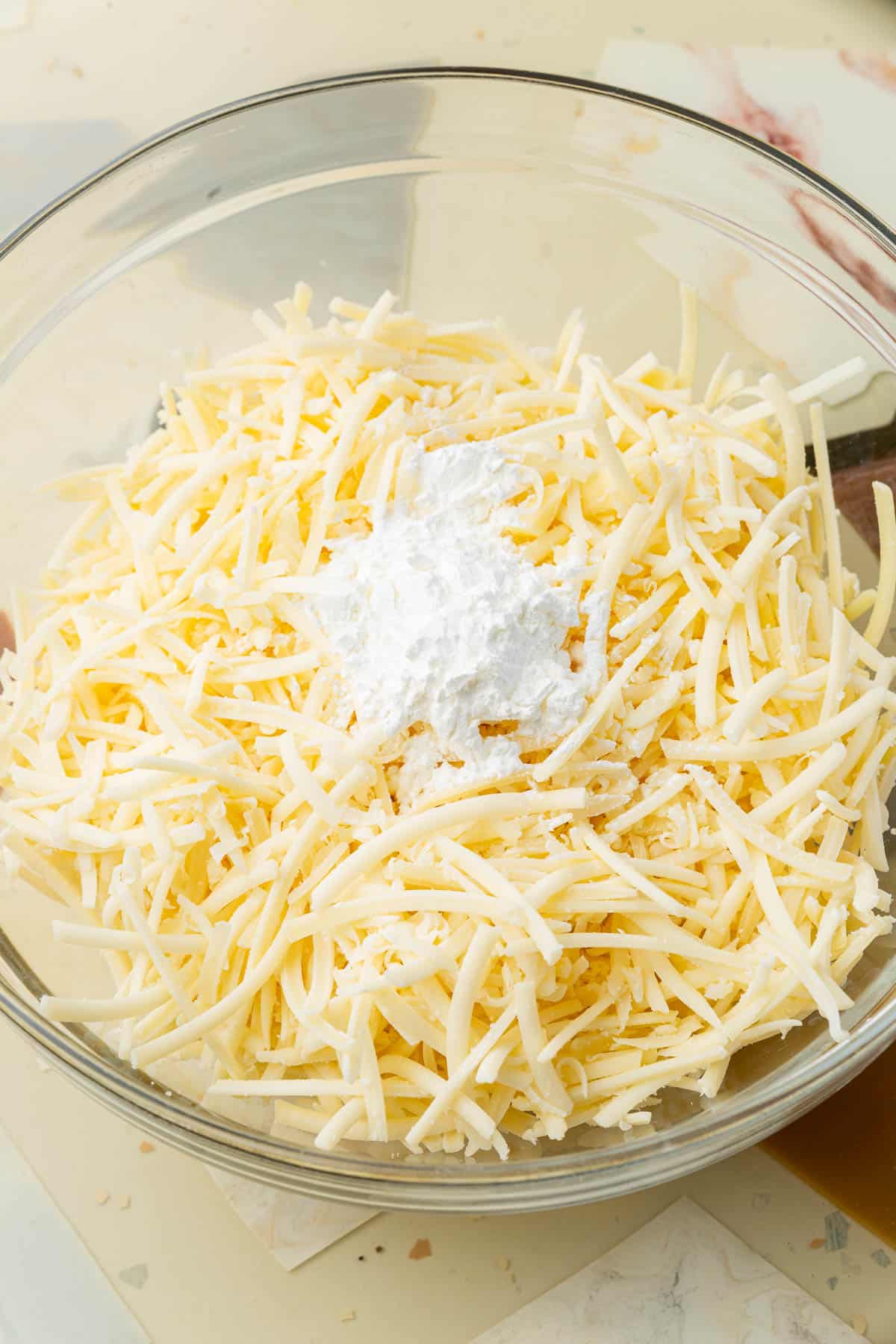A glass bowl of Emmental and Gruyère cheese topped with a few tablespoons of cornstarch.