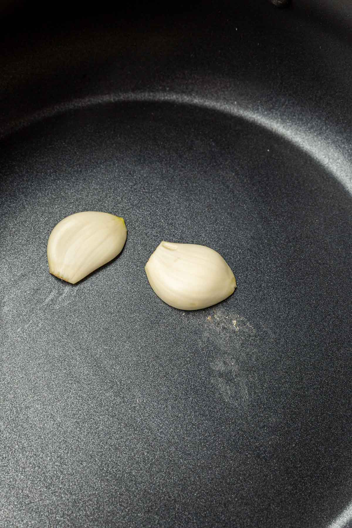 Two garlic cloves being rubbed on the interior of an electric fondue pot.