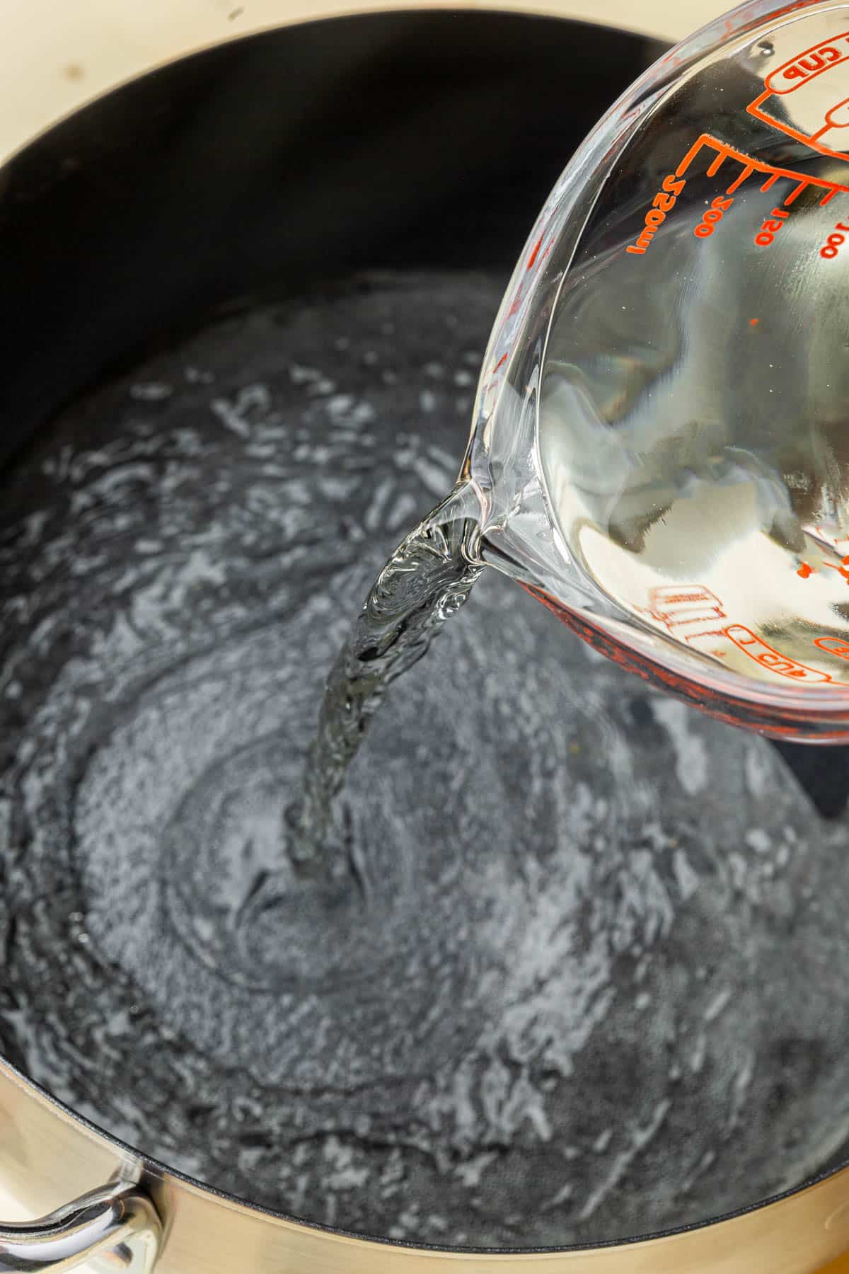 A measuring cup pouring white wine into an electric fondue pot.