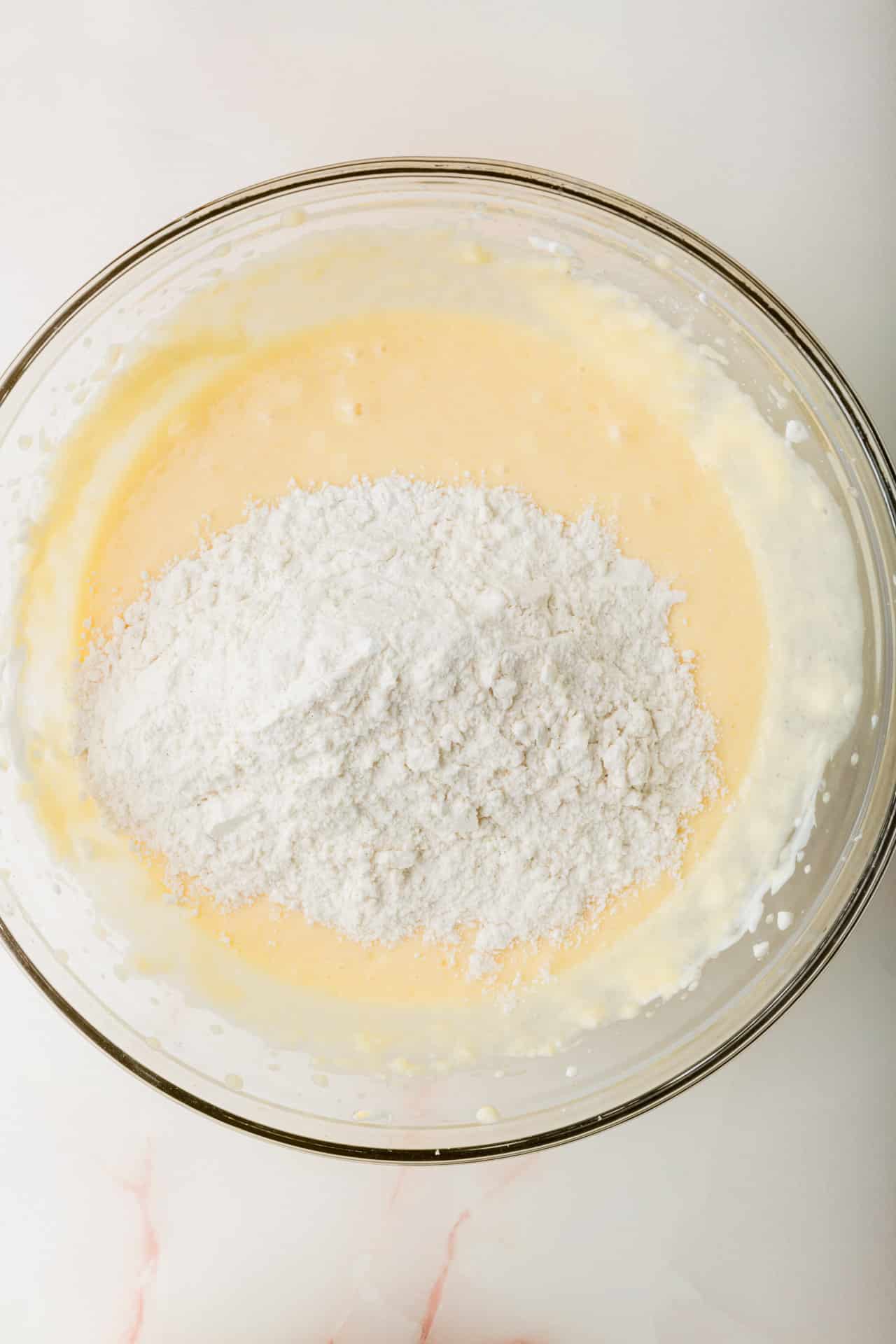 A glass mixing bowl with gluten-free flour on top of wet ingredients to make coffee cake.