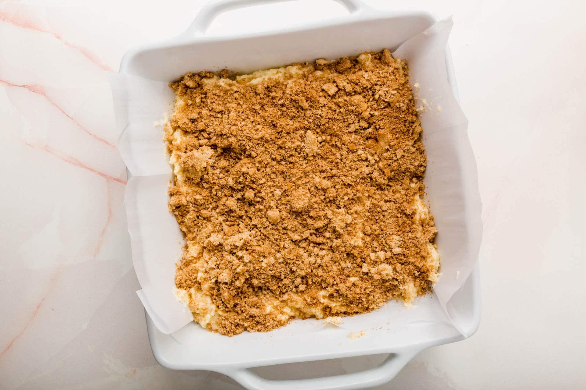 A white baking dish with coffee cake batter topped with streusel before baking in the oven.