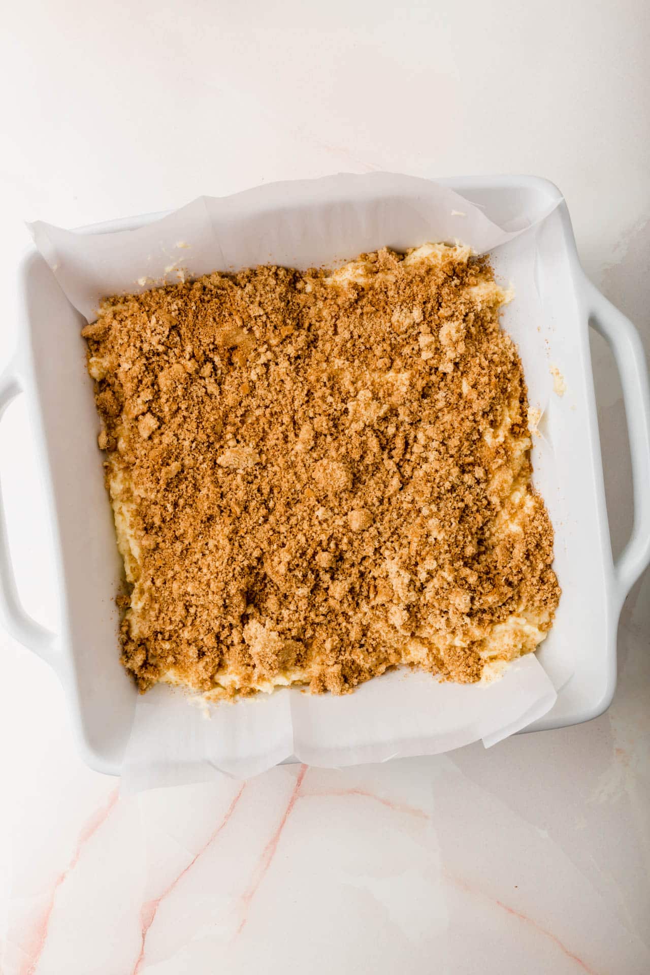 A white baking dish with coffee cake batter topped with streusel before baking in the oven.
