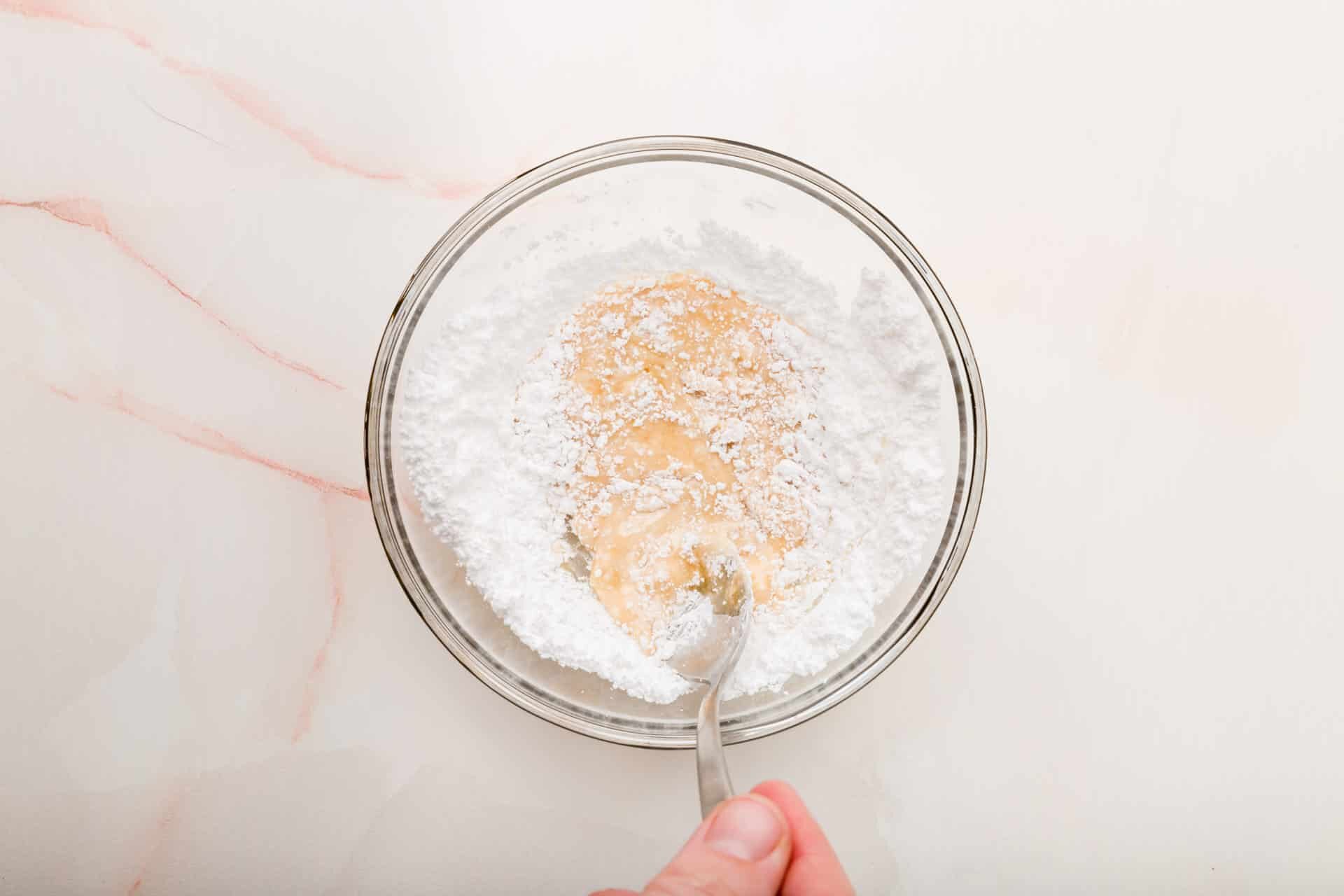 A small bowl with powdered sugar, milk and vanilla being mixed together with a spoon.