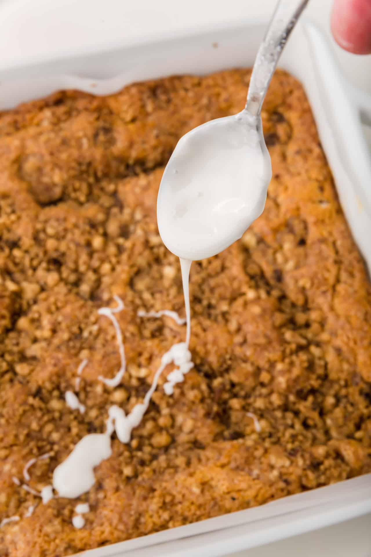 A spoon drizzling a powdered sugar glaze over a gluten-free coffee cake.