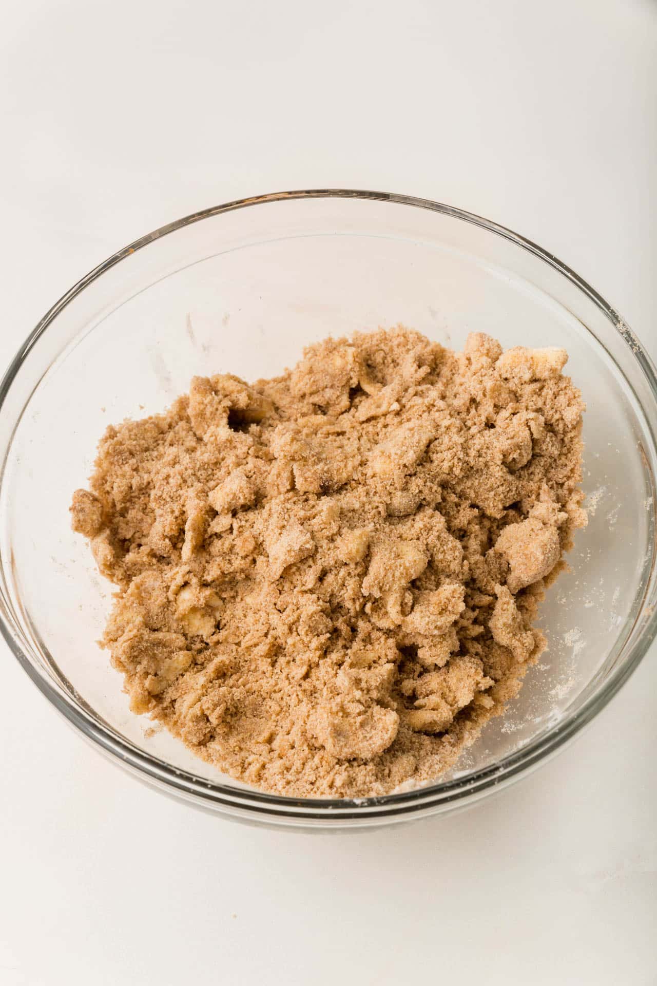 A glass mixing bowl with brown sugar, cinnamon, and cold butter mixed together to make a streusel.