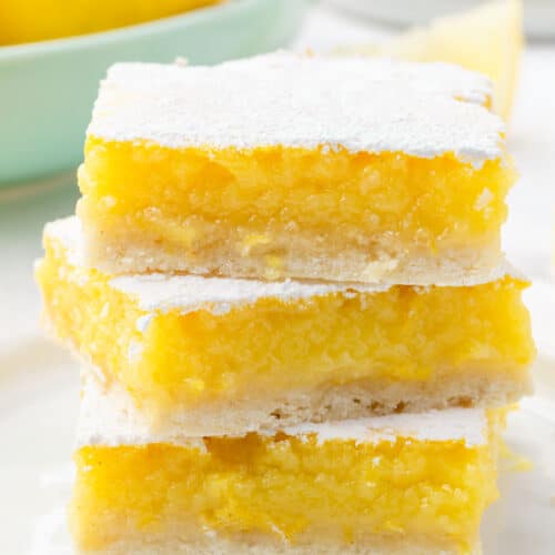 A stack of three gluten free lemon bars on a dessert plate with a bowl of lemons in the background.