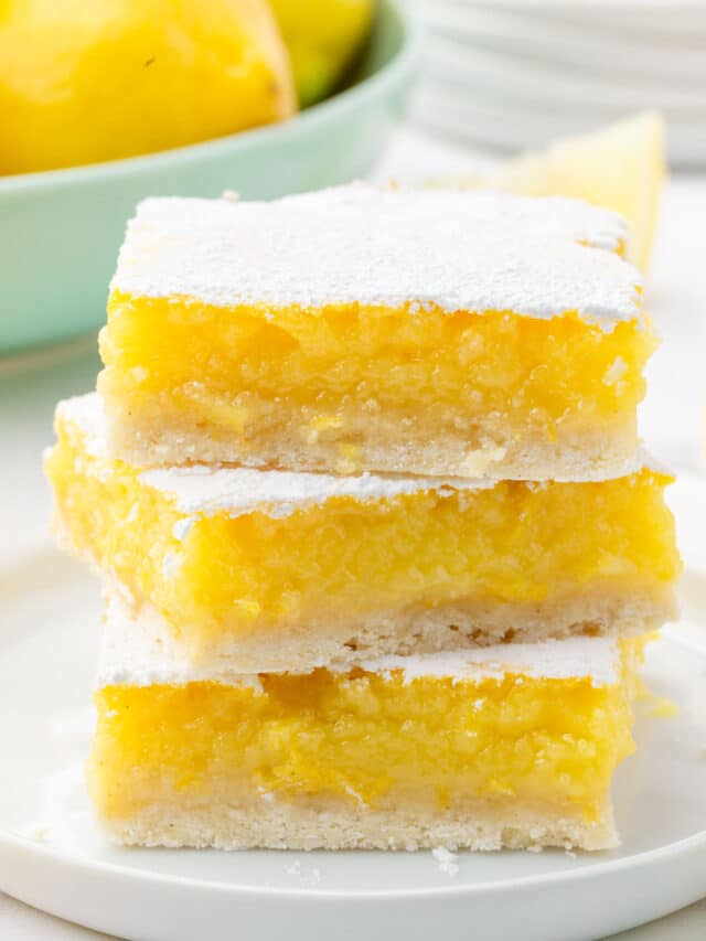 A stack of three gluten free lemon bars on a dessert plate with a bowl of lemons in the background.