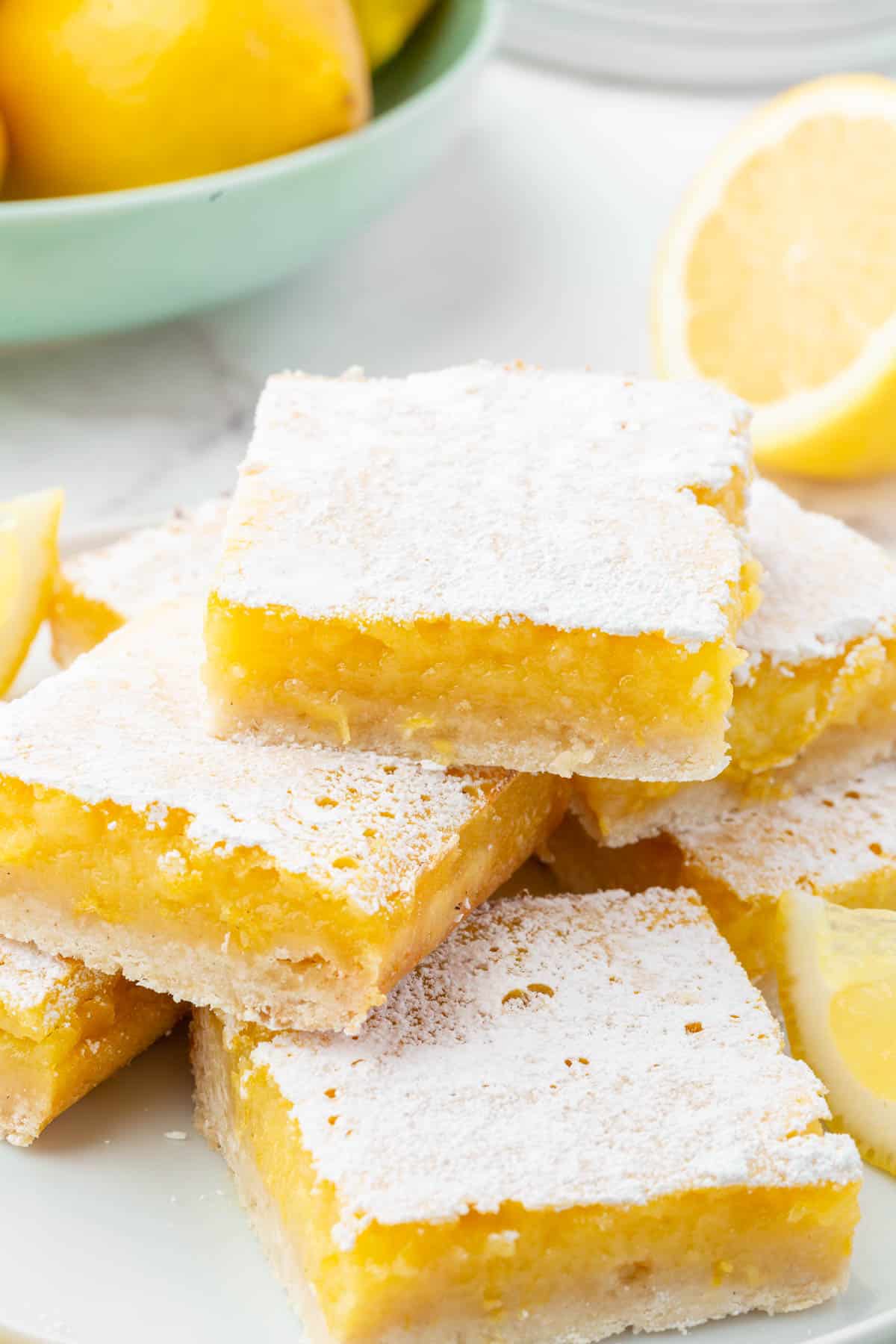 Gluten free lemon slices stacked on top of each other on a plate with a blue bowl of lemons in the background.