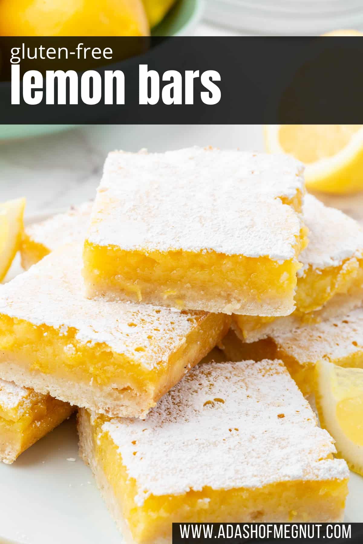 Stacks of gluten free lemon slices on a plate that have been dusted with powdered sugar with lemons in the background.