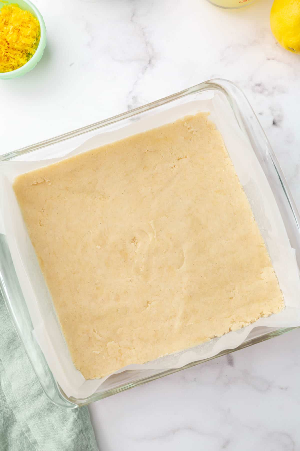 A square glass baking dish with a gluten free shortbread dough in it before baking in the oven.