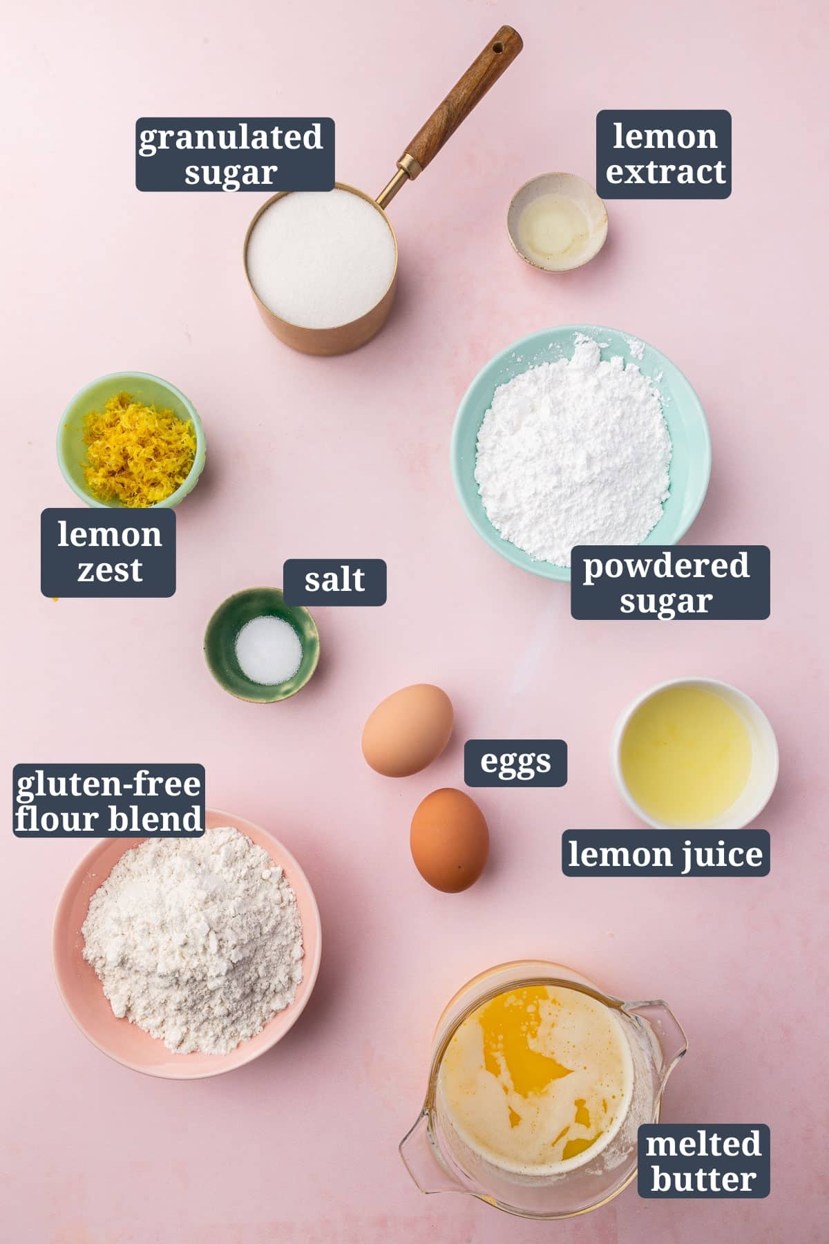 An overhead view of ingredients in bowls to make gluten free lemon brownies, including granulated sugar, lemon extract, lemon zest, salt, powdered sugar, eggs, lemon juice, gluten-free flour blend, and melted butter with text overlays over each ingredient.