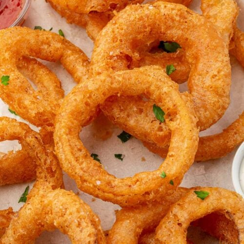 A close up of gluten free onion rings topped with parsley on a parchment lined baking sheet with ketchup peaking in.