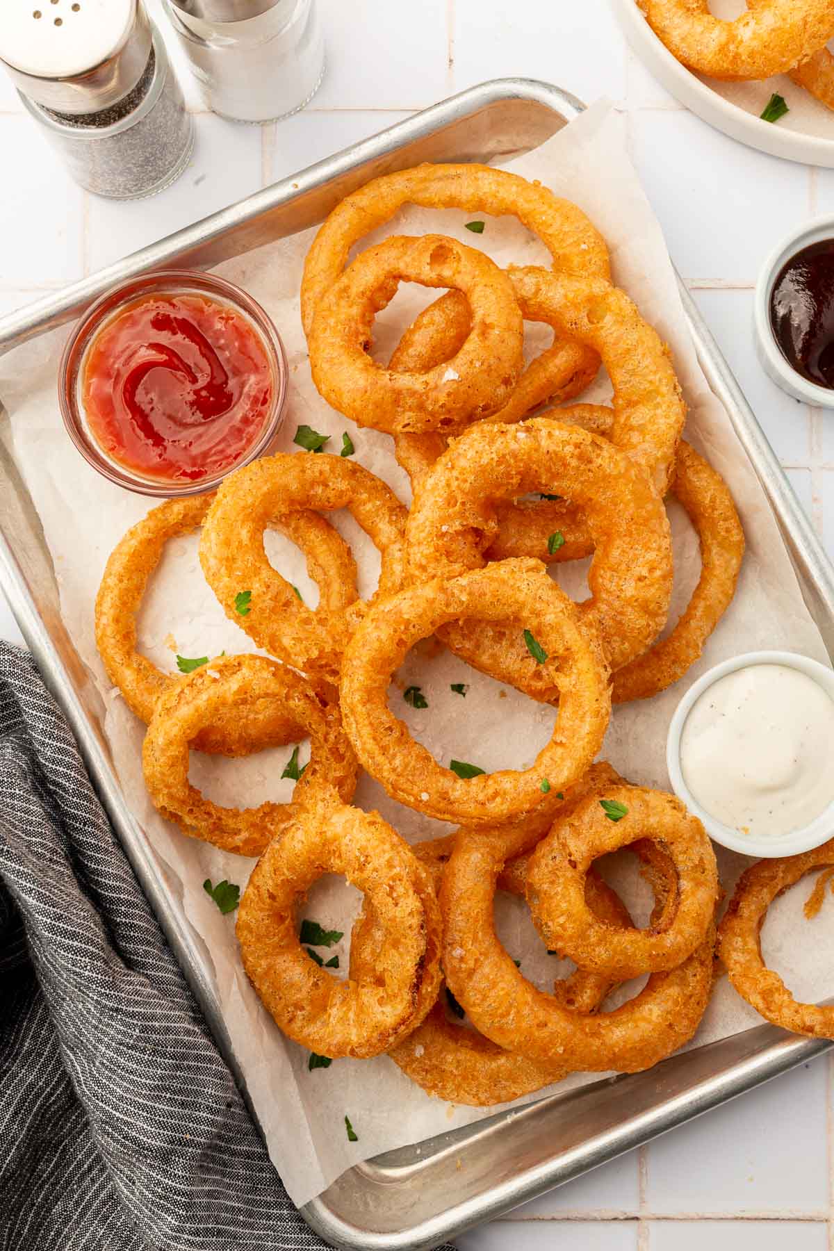 Gluten-free onion rings on a parchment lined baking sheet with a ramekin of ranch and a ramekin of ketchup.