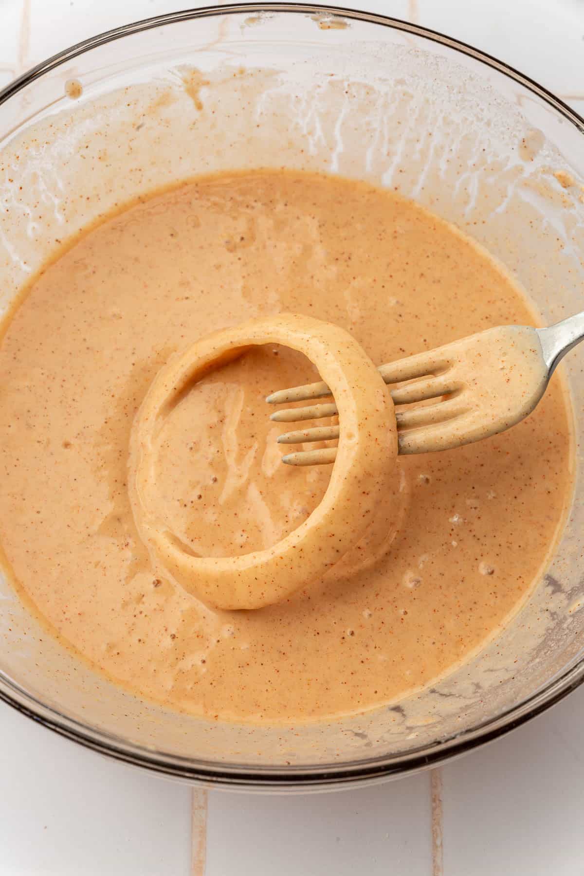 An onion ring dipped in gluten-free batter with a fork.