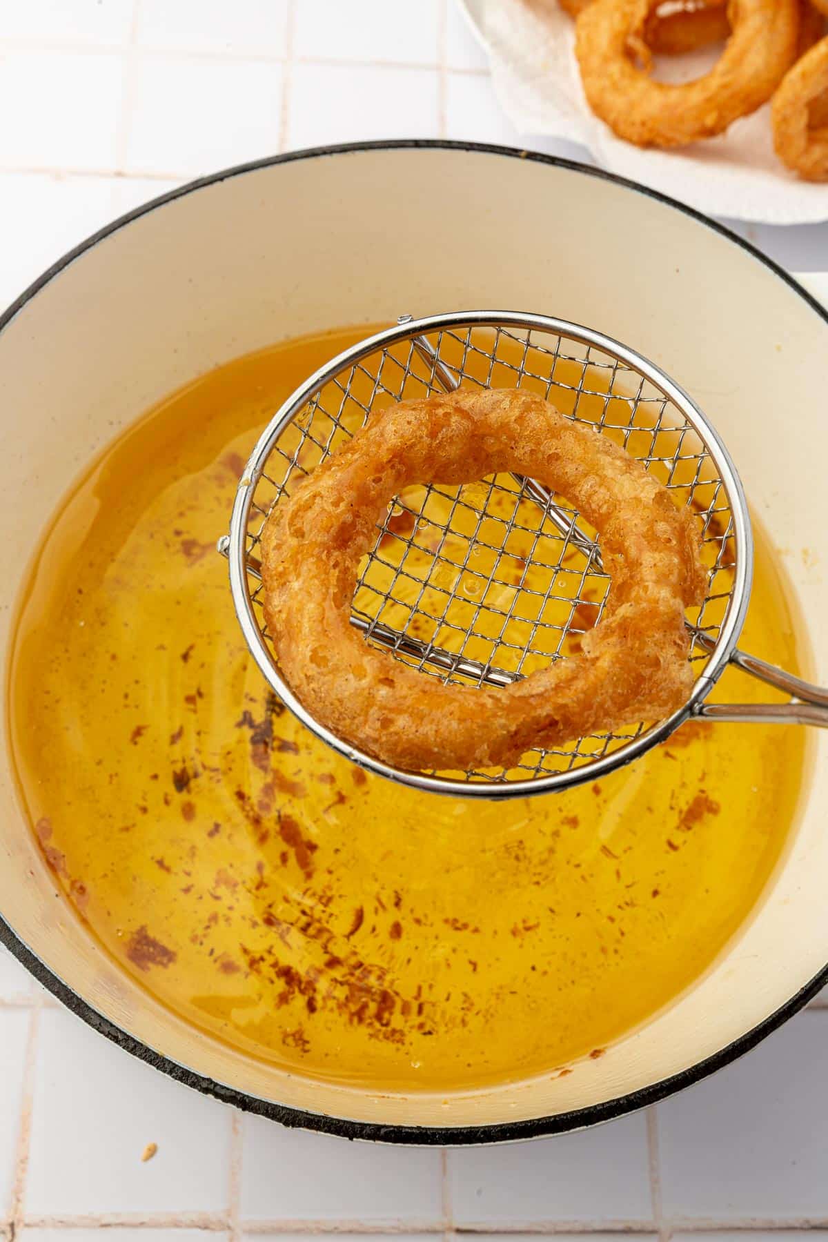 A wire spider spatula removing a gluten free onion ring from a pot of hot oil.