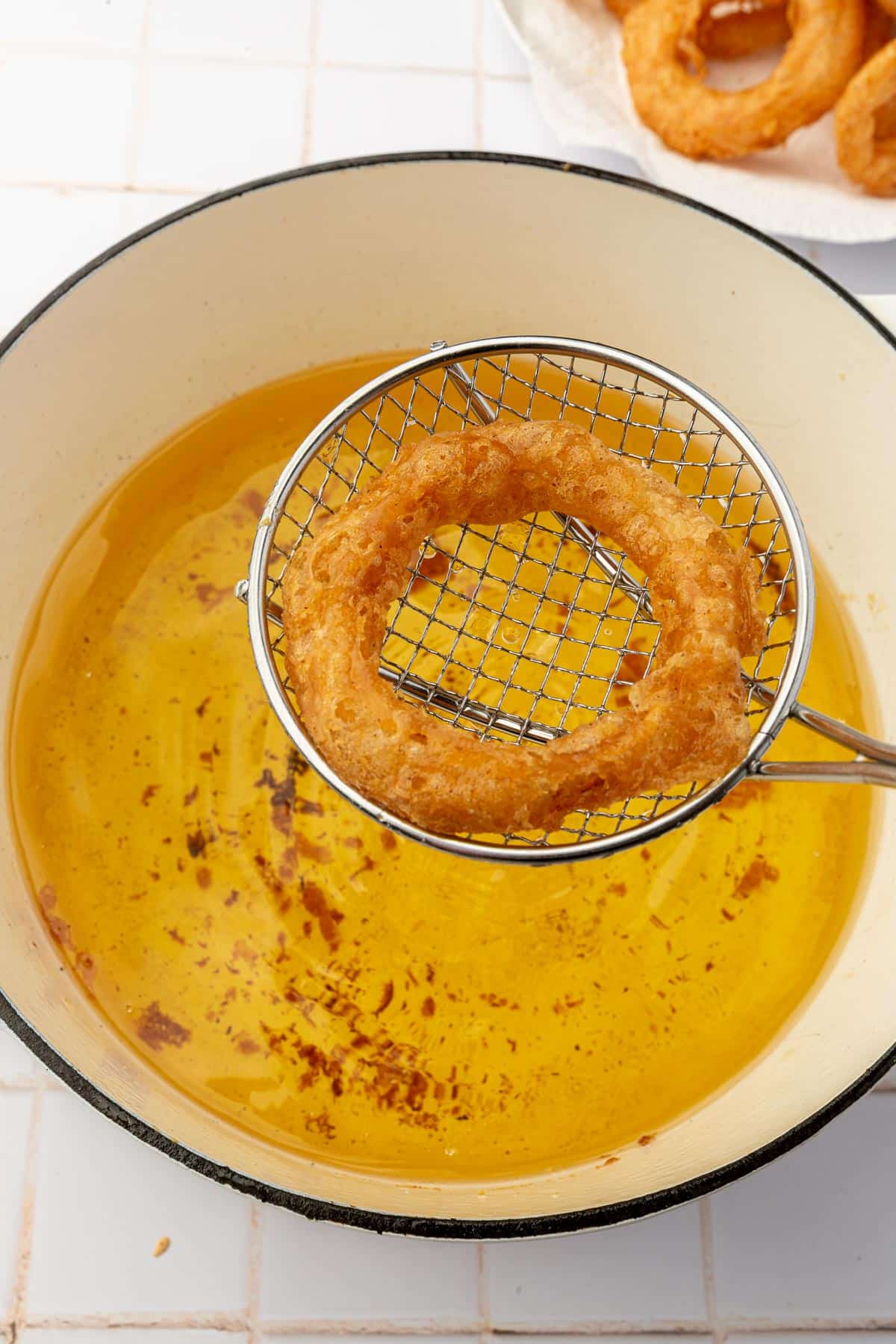 A wire spider spatula removing a gluten free onion ring from a pot of hot oil.
