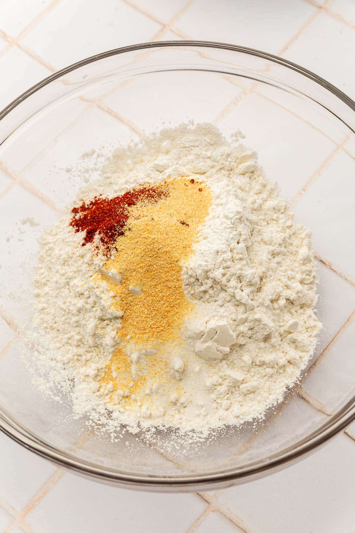 A glass mixing bowl with gluten-free flour blend, garlic powder, paprika and salt before mixing together.