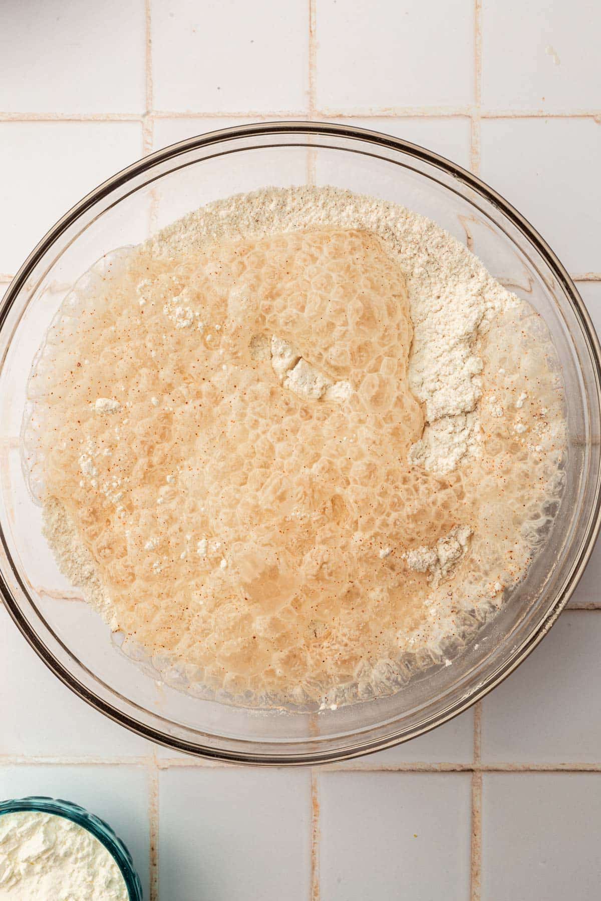 A glass mixing bowl with a gluten-free flour blend topped with club soda that has began to bubble up.