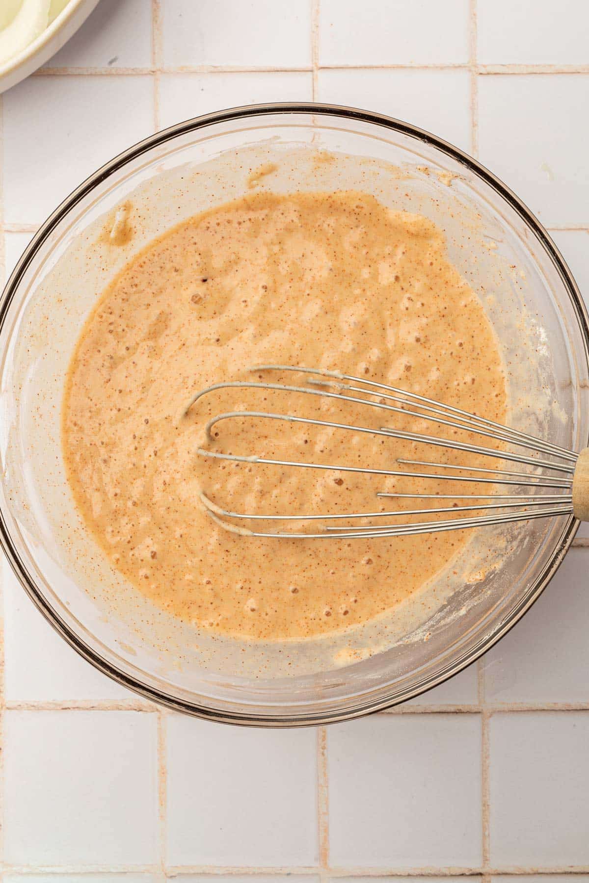 A glass mixing bowl with gluten-free batter and a whisk.