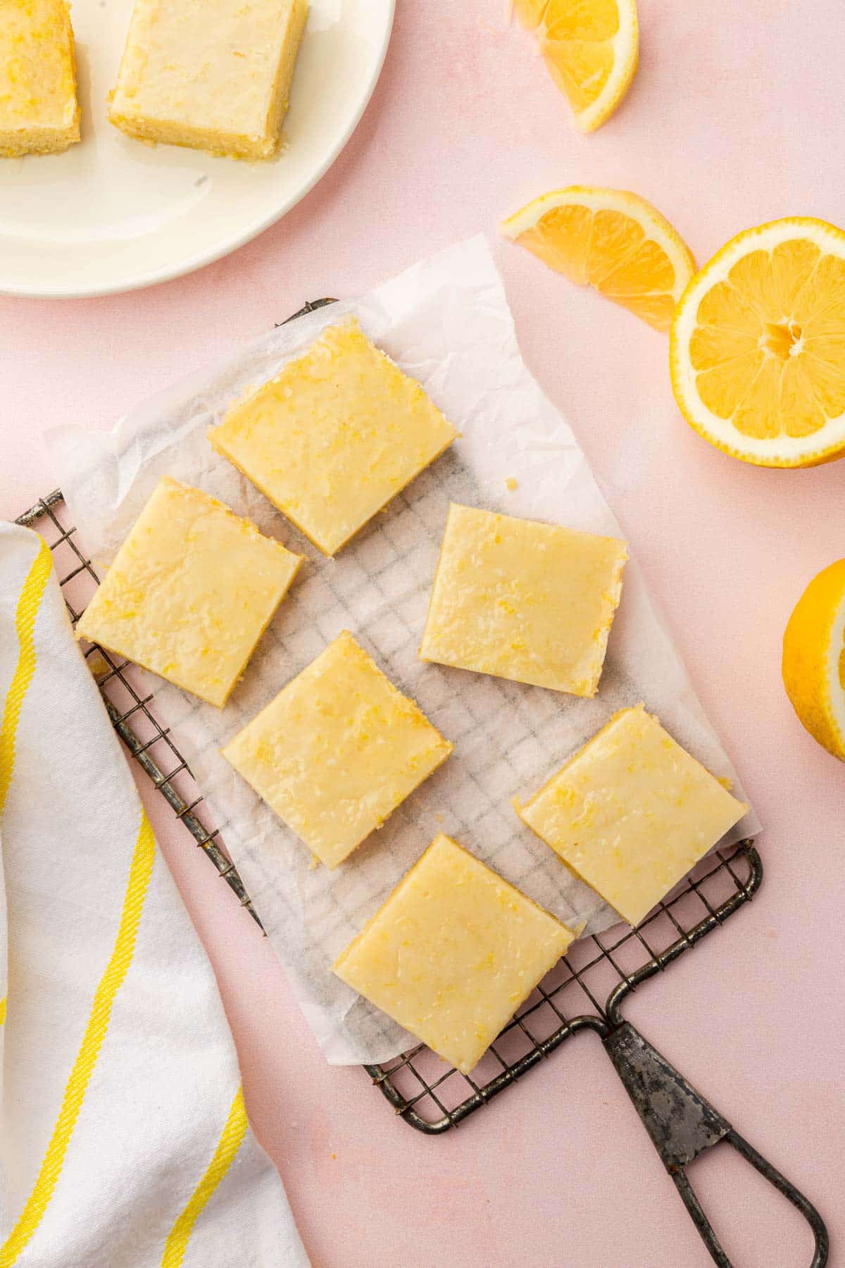 An overhead view of gf lemon brownies on a cooling rack with parchment paper with fresh lemon halves and slices on the side.