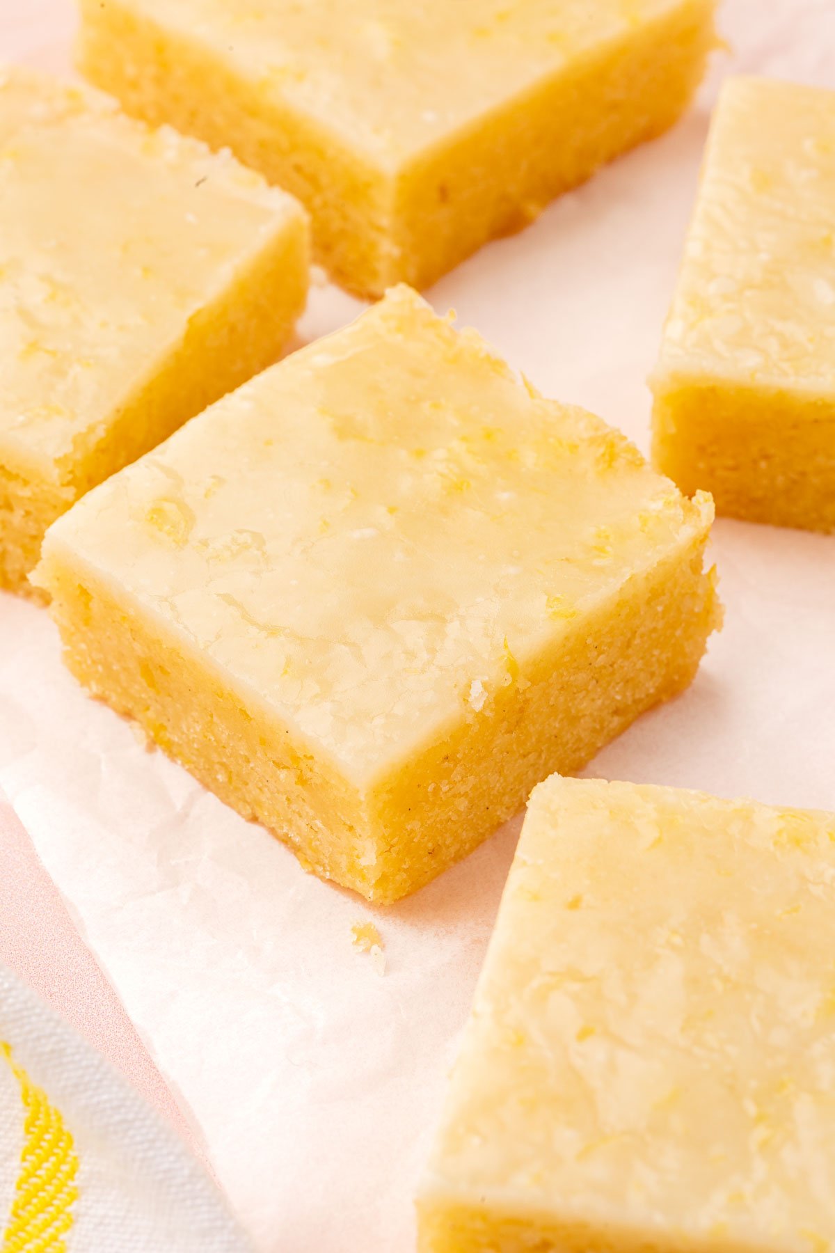 Square of gluten free lemon brownies with lemon glaze on a piece of parchment paper.