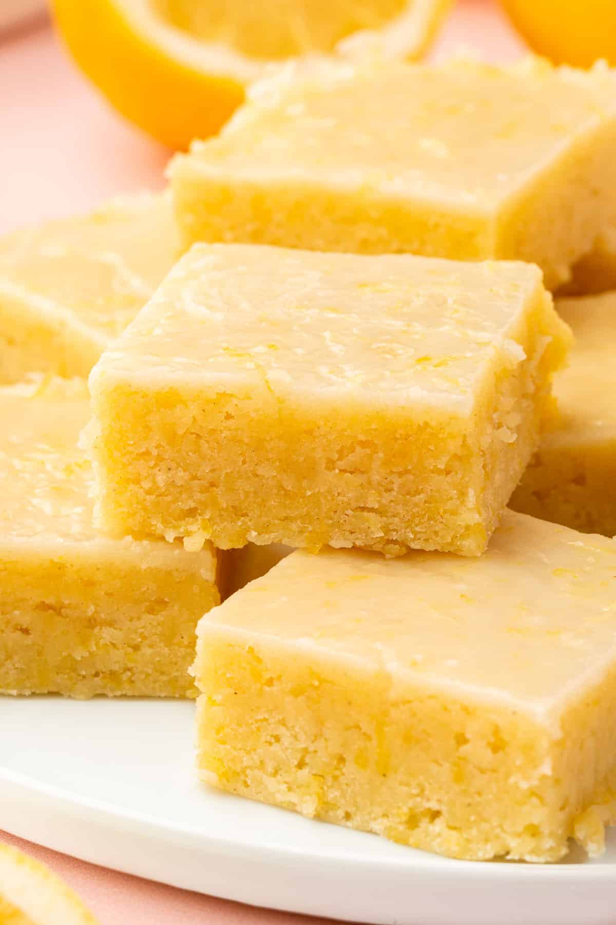 A stack of gluten free lemon brownies with lemon glaze on a white dessert plate.