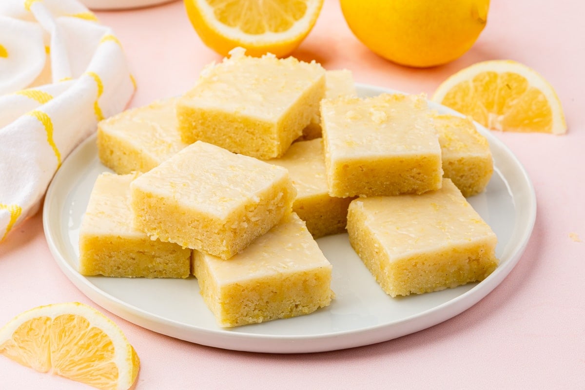 A plate of gluten-free lemon brownies that have been stacked with lemon halves and wedges surrounding the plate.