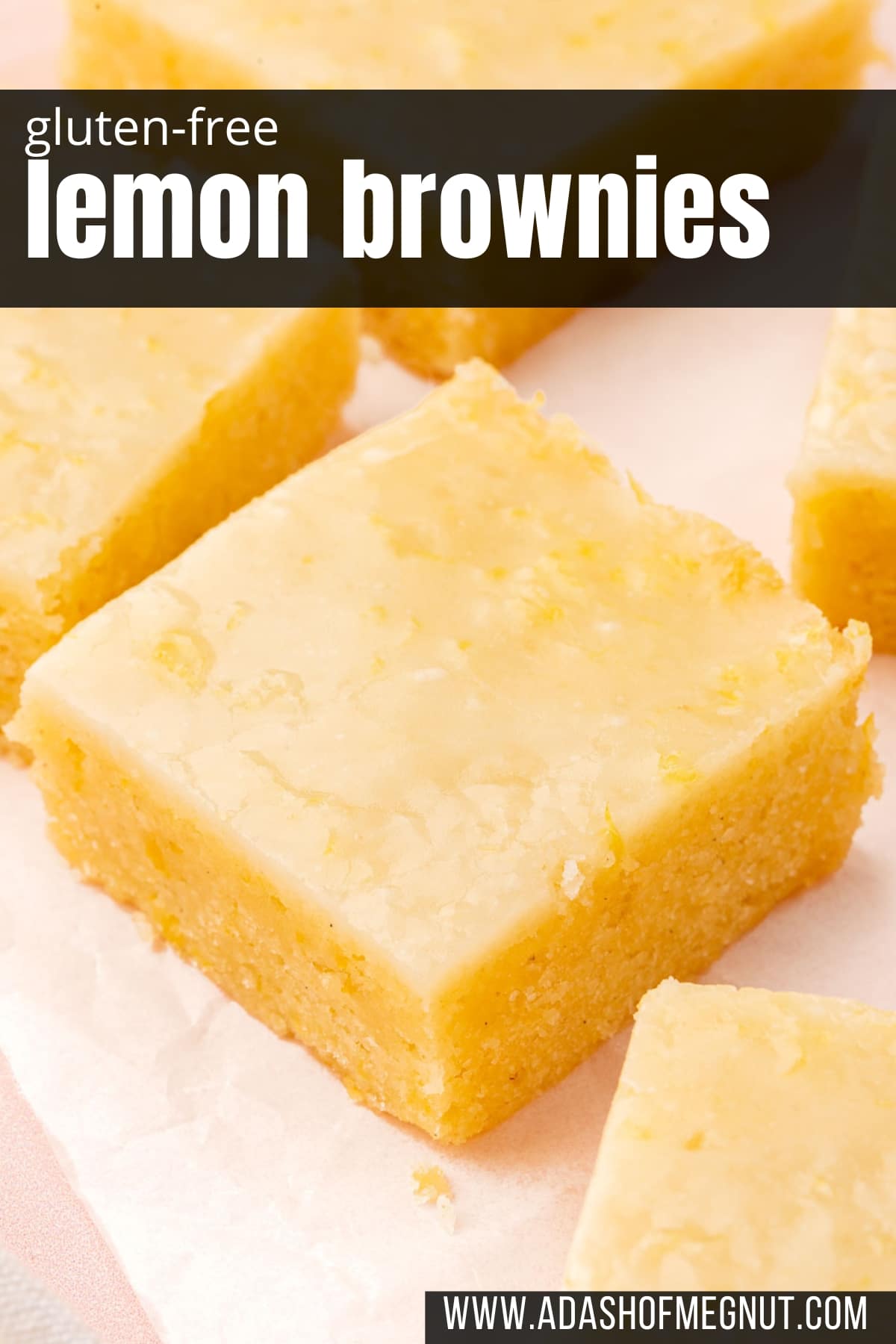 A closeup of a lemon brownie square on a piece of parchment paper with additional brownies surrounding.