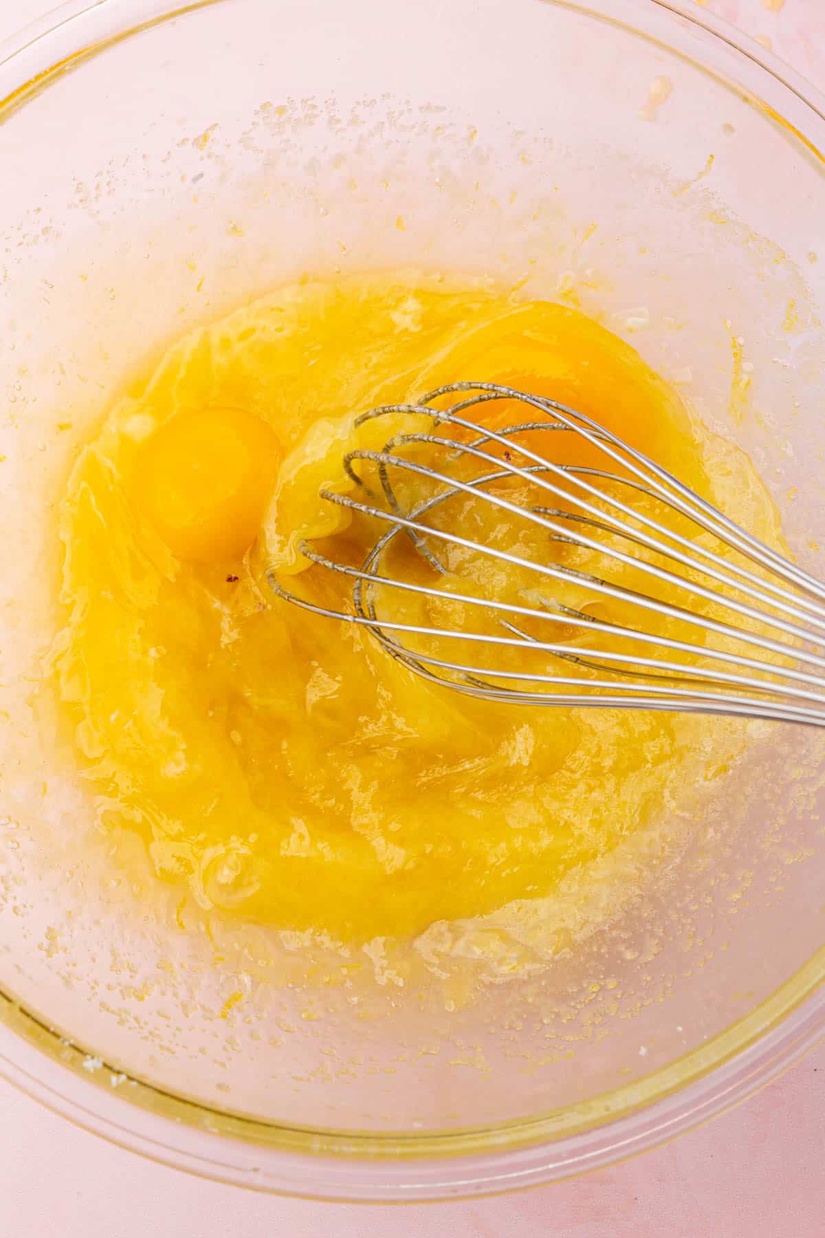 A glass mixing bowl with a melted butter, lemon juice and egg mixture that is been whisked.