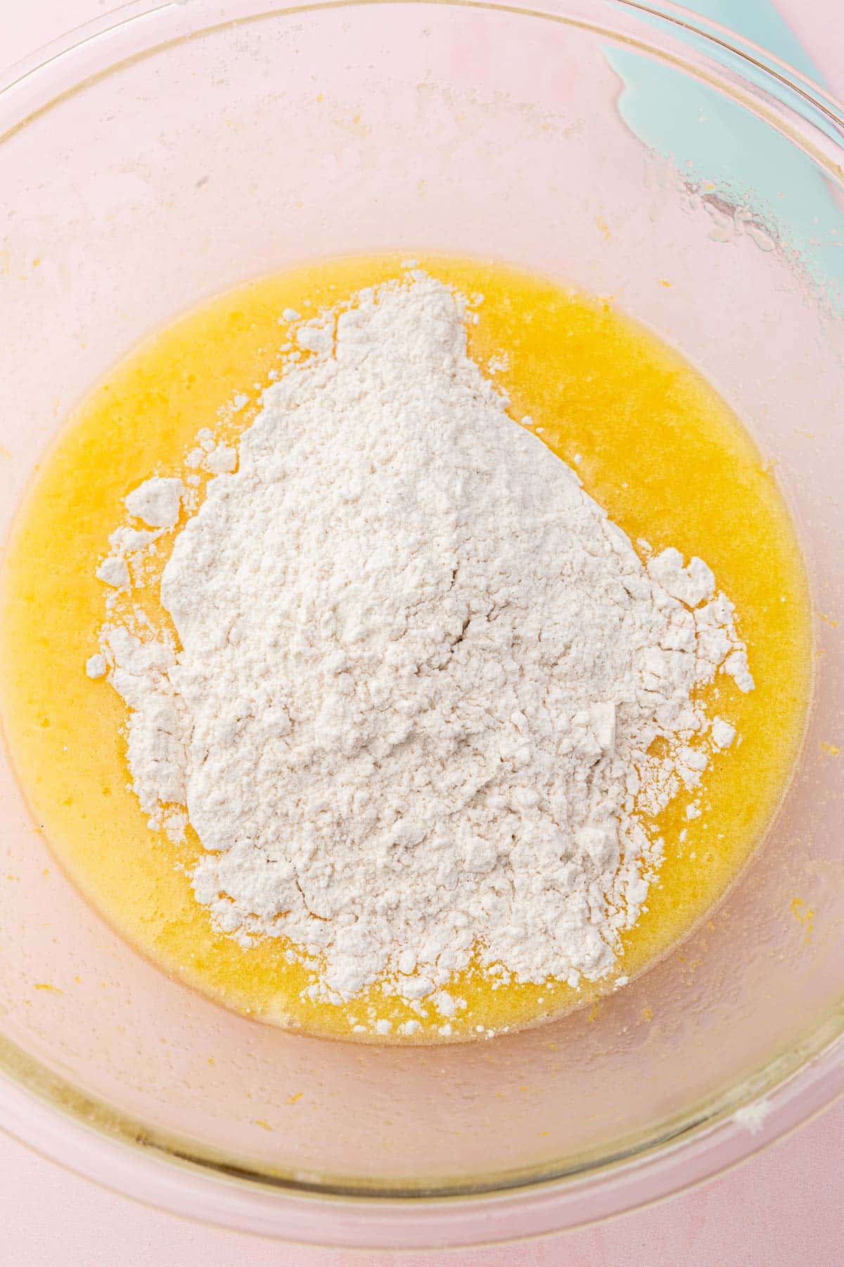 A glass mixing bowl with a lemon mixture topped with gluten-free flour before mixing together.