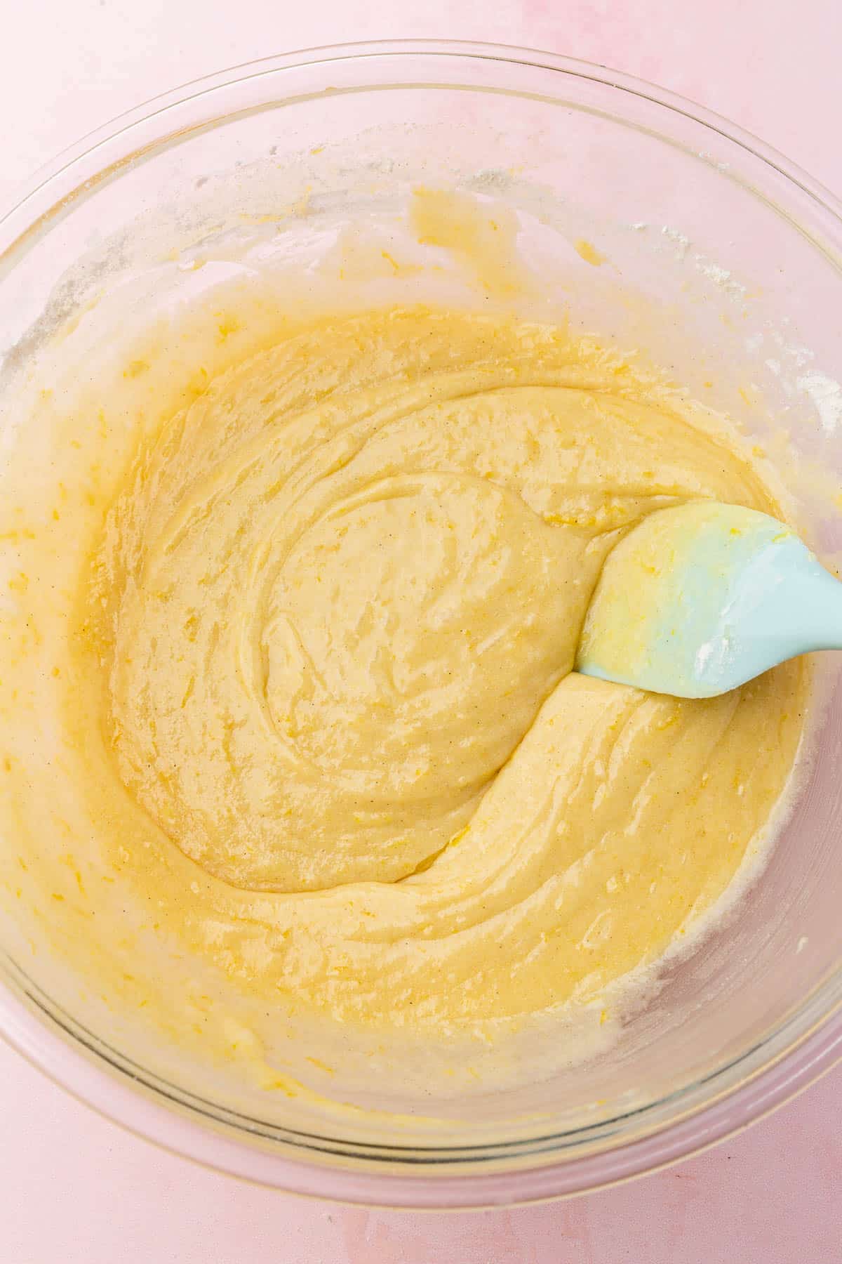 A glass mixing bowl of gluten-free lemon brownie batter with a blue spatula.