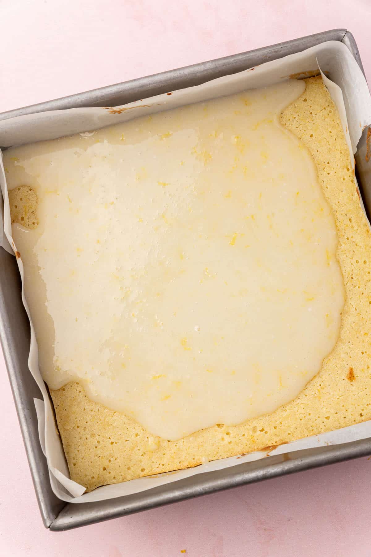 A square metal baking dish with lemon brownies that have been partially covered with lemon glaze.