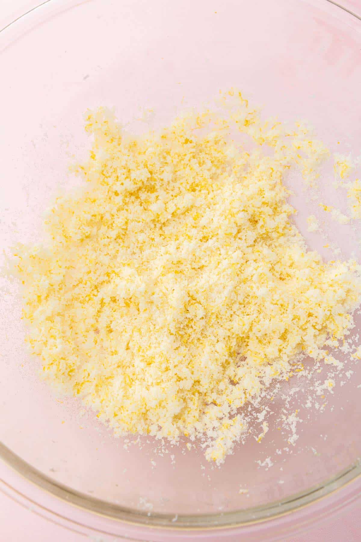 A glass mixing bowl with a granulated sugar and lemon zest mixture that has been mixed together.