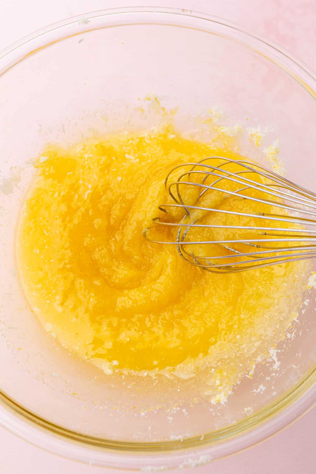 A glass mixing bowl with melted butter and granulated sugar that is being whisked together.