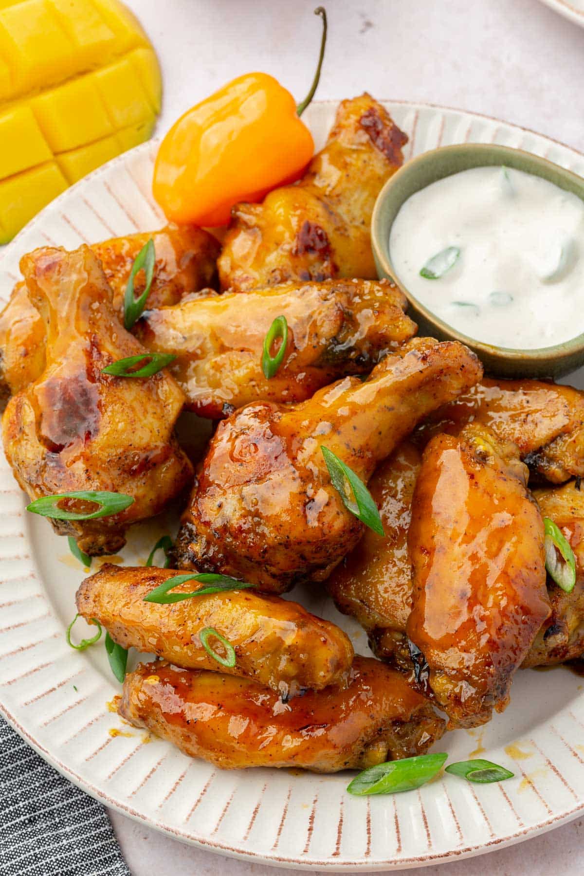 A close up of mango habanero wings with a ramekin of bleu cheese dressing to the side topped with green onions.